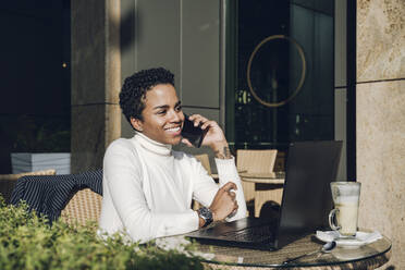Lächelnde Geschäftsfrau, die in einem Restaurant über ihr Smartphone spricht - VYF00312