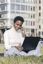 Smiling businesswoman with laptop sitting at public park in city - VYF00316
