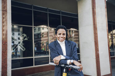 Lächelnde Geschäftsfrau mit Elektro-Scooter in der Stadt - VYF00323