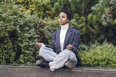 Thoughtful young businesswoman looking away while practicing yoga on retaining wall - VYF00340