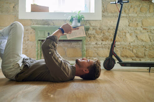 Caucasian man lying on floor while reading book in living room - KIJF03390