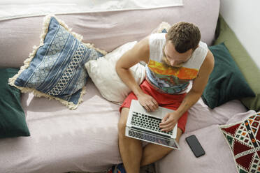 Mann mit Laptop auf Sofa im Wohnzimmer zu Hause - IFRF00110