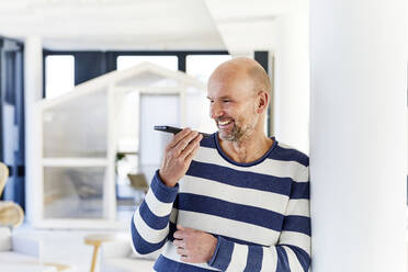 Lächelnder Mann, der zu Hause steht und mit seinem Handy spricht - FMKF06756