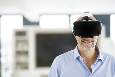 Businessman using virtual reality headset while standing at home - FMKF06759