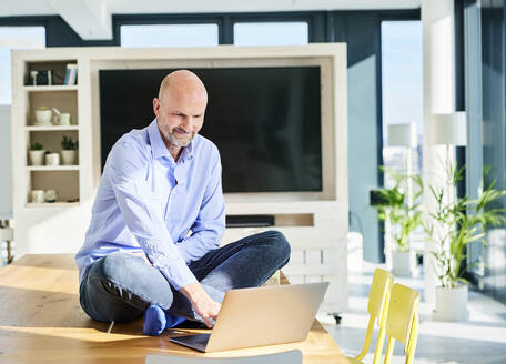 Älterer Geschäftsmann arbeitet am Laptop, während er zu Hause am Tisch sitzt - FMKF06775