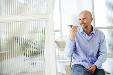 Mature businessman smiling while talking on mobile phone at home - FMKF06784