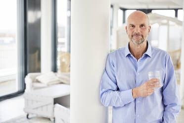 Businessman holding drinking glass while standing at home - FMKF06786