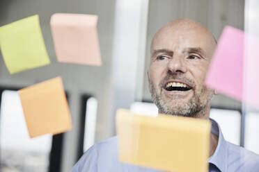 Mature businessman reading sticky note on glass wall - FMKF06800