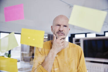 Confused man with hand on chin reading adhesive note - FMKF06804