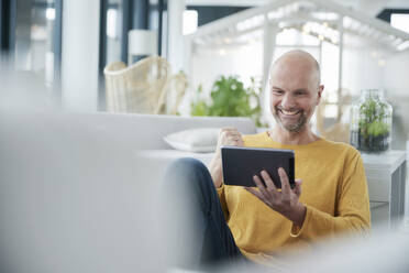 Lächelnder Mann jubelt, während er ein digitales Tablet zu Hause benutzt - FMKF06811
