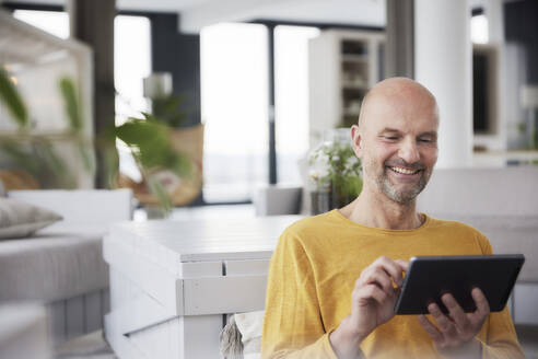 Lächelnder Mann, der ein digitales Tablet benutzt, während er zu Hause sitzt - FMKF06813