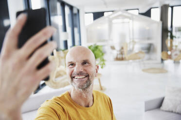 Mann, der ein Selfie mit seinem Smartphone macht, während er zu Hause steht - FMKF06814