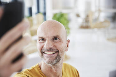 Älterer Mann, der ein Selfie mit seinem Smartphone macht, während er zu Hause steht - FMKF06815