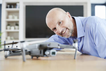 Lächelnder Geschäftsmann, der einen Quadcopter untersucht, während er zu Hause steht - FMKF06818