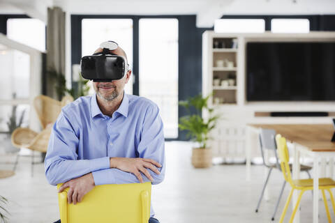Smiling businessman using virtual reality headset while sitting on chair at home stock photo
