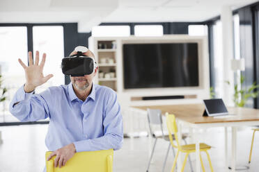 Businessman wearing virtual reality headset touching while sitting on chair - FMKF06824