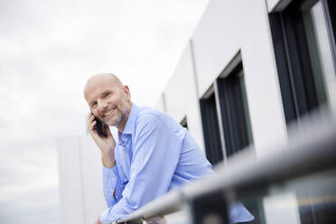 Geschäftsmann, der auf dem Dach stehend mit seinem Mobiltelefon telefoniert - FMKF06831