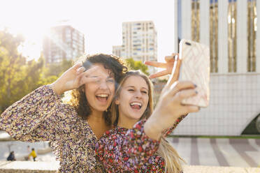 Fröhliche Freundinnen machen ein Friedenszeichen, während sie ein Selfie mit ihrem Smartphone in der Stadt machen - IFRF00140