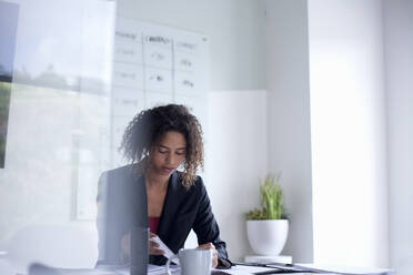 Businesswoman with document on desk sitting in office - AJOF00791