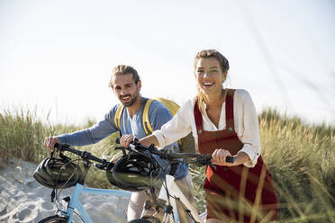 Young man and woman walking with bicycles against clear sky - UUF22194