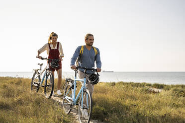 Man and woman walking with bicycles against clear sky - UUF22201