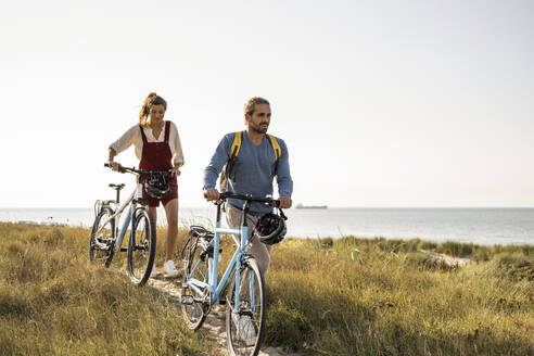 Mann und Frau zu Fuß mit Fahrrädern gegen den klaren Himmel - UUF22201