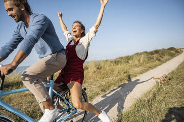 Carefree woman enjoying bicycle ride with man against clear sky - UUF22205