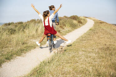 Carefree girlfriend enjoying bicycle ride with boyfriend on sunny day - UUF22208