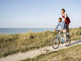 Young woman enjoying ride with man while standing on bicycle against clear sky - UUF22209