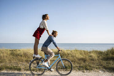 Girlfriend enjoying ride with man while standing on bicycle against clear sky - UUF22211