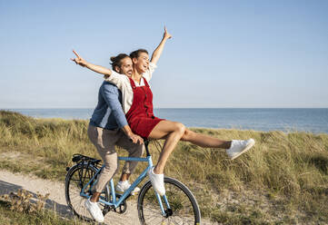 Carefree couple enjoying bicycle ride against clear sky - UUF22214