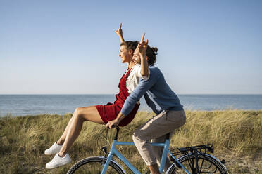 Happy couple enjoying bicycle ride together against clear sky - UUF22215