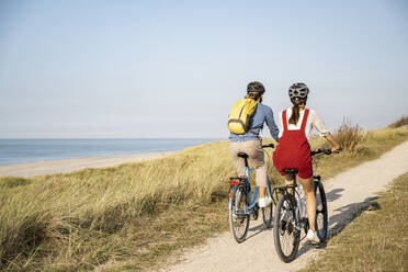 Young couple wearing cycling helmet riding bicycles against clear sky - UUF22216