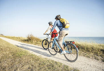 Man with backpack cycling bicycle with woman on footpath during sunny day - UUF22217