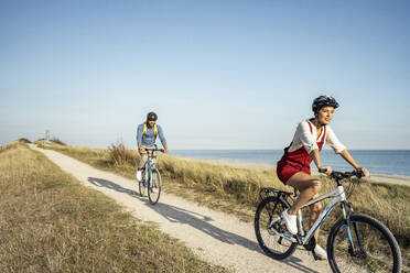 Mann und Frau mit Fahrradhelm fahren an einem sonnigen Tag Fahrrad - UUF22221