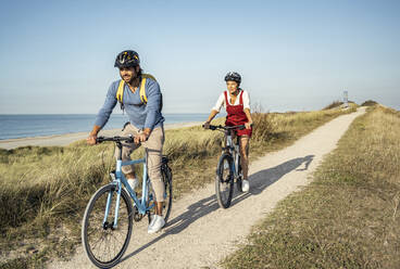 Girlfriend and boyfriend riding bicycles on sunny day against clear sky - UUF22222