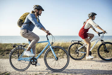 Couple wearing helmet riding bicycles against sea - UUF22224