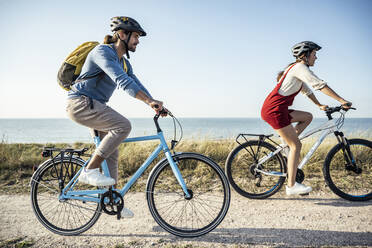 Pärchen mit Helm auf Fahrrädern gegen das Meer - UUF22224