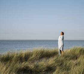 Young woman wrapped in shawl standing against clear sky - UUF22227