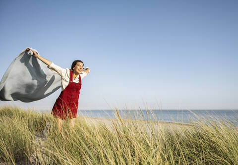 Young woman with arms outstretched holding shawl while standing at beach stock photo