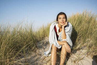 Nachdenkliche Frau mit Hand am Kinn, die wegschaut, während sie am Strand sitzt - UUF22232