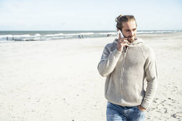 Lächelnder Mann schaut weg, während er am Strand mit seinem Handy telefoniert - UUF22235