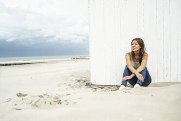 Lächelnde Frau, die wegschaut, während sie am Strand sitzt - UUF22241