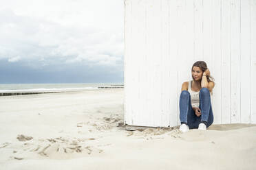 Junge Frau schaut weg, während sie am Strand sitzt - UUF22242