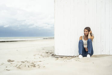 Young woman looking away while sitting at beach - UUF22242