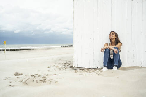Frau entspannt mit geschlossenen Augen am Strand sitzend - UUF22243