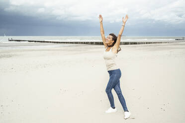 Young woman with arms raised dancing while dancing at beach - UUF22246