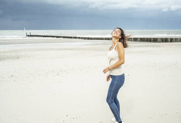 Smiling woman standing with eyes closed at beach - UUF22247