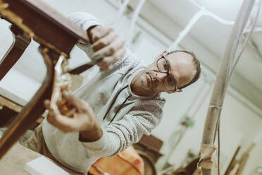 Männlicher Experte, der Goldfarbe auf antike Möbel aufträgt, in einer Werkstatt - OCAF00557