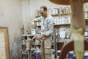 Handwerker, der weiße Farbe in eine Spritzpistole einfüllt, während er in der Werkstatt steht - OCAF00570